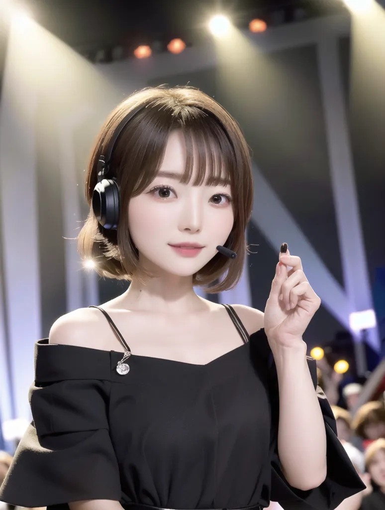 Gambar ini menunjukkan seorang wanita muda dengan rambut coklat pendek dan mata coklat. Dia mengenakan gaun hitam off-the-shoulder dan sepasang headphone hitam. Dia memegang mikrofon di tangan kanannya dan mengangkat tangan kirinya ke udara. Dia berdiri di depan kerumunan orang yang bersorak dan melambai-lambaikan tangan mereka. Latar belakangnya adalah panggung besar dengan lampu terang.