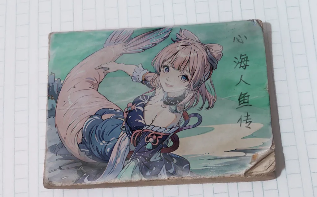 The image shows a colorful illustration of a mermaid. She has pink hair and blue eyes, and is wearing a blue and white kimono. She is sitting on a rock in the ocean, and is smiling at the viewer. The illustration is drawn in a traditional Japanese style, and is very detailed. The colors are vibrant and the lines are clean. The image is also very well composed, and the mermaid is placed in the center of the frame. The overall effect is one of beauty and serenity.