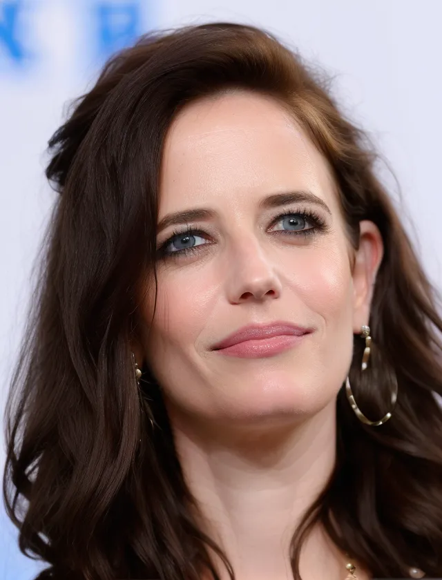 The image shows a headshot of Eva Green, a French actress. She has long, dark brown hair with bangs, and her eyes are a light blue color. She is wearing a light pink blush and lipstick, and her skin is flawless. She is wearing a white button-down shirt, and she has a hoop earring in her left ear. She is looking at the camera with a slight smile on her face.