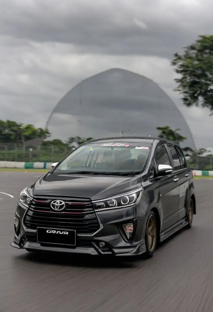 The image shows a black car with a sporty design. It is driving on a race track with a large building in the background. The car has a sleek and aerodynamic design, with a large front grille and sharp headlights. The car is also equipped with a rear spoiler and a set of alloy wheels. The car is likely to be a high-performance model, as it is equipped with a number of features that are designed to improve its performance.