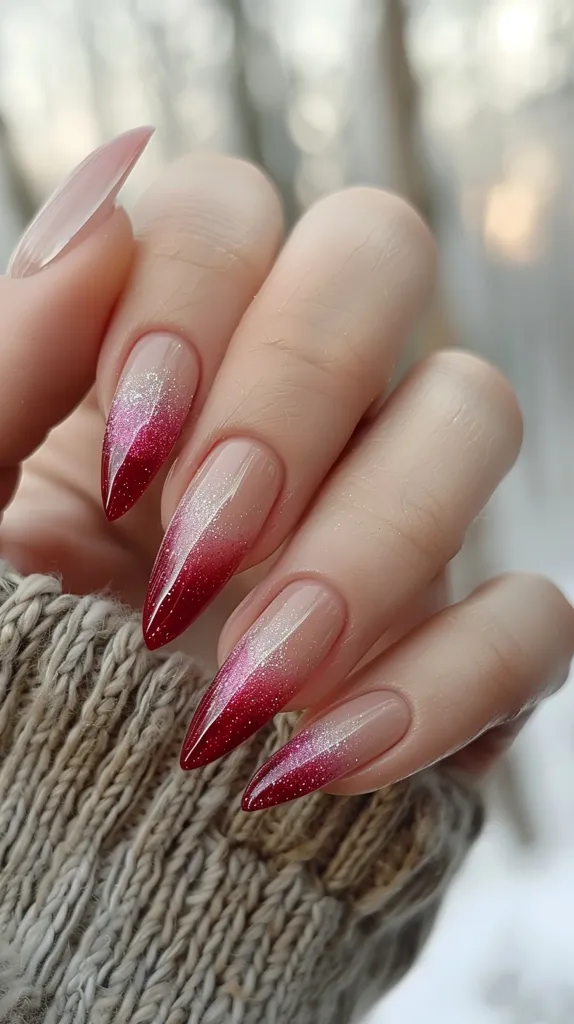 The image shows a hand with long, stiletto-shaped nails. The nails are painted with a red and silver glitter ombre design. The ombre starts with a light silver at the base of the nails and transitions to a deep red at the tips. The nails are also filed into a sharp point. The hand is holding a white rose. The background is a close-up of a white rose.