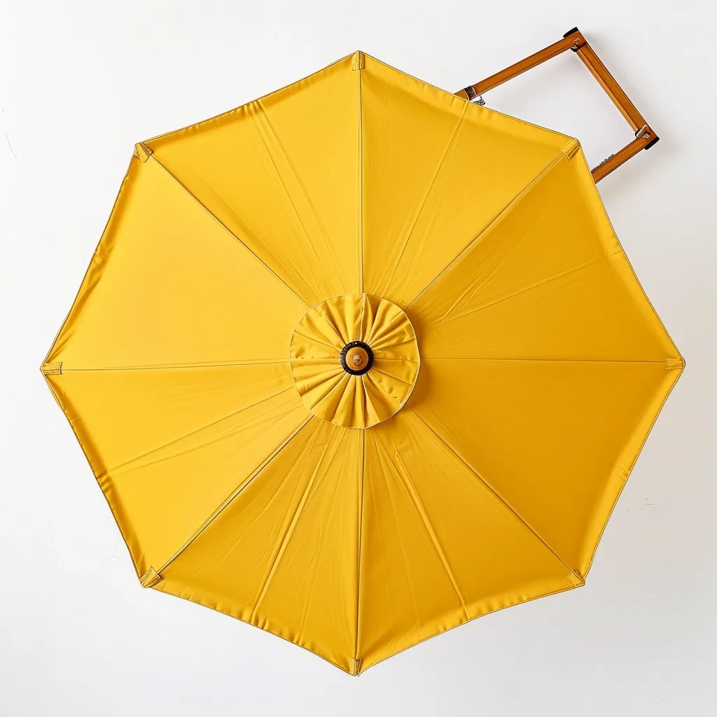 The image shows a vibrant yellow umbrella, closed and resting on a white surface. It has a wooden frame and a central, circular embellishment with a brown button in the middle. The umbrella casts a shadow against the white background, creating a clean and minimalist composition. The bright color of the umbrella pops against the white backdrop.