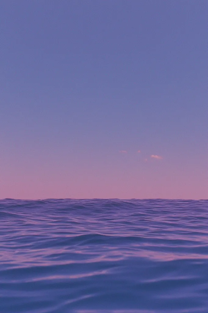 The image depicts a serene seascape at dusk. The sky is a soft gradient of purple and pink, with a few wispy clouds.  The calm ocean water reflects the colors of the sky, creating a tranquil and peaceful atmosphere.