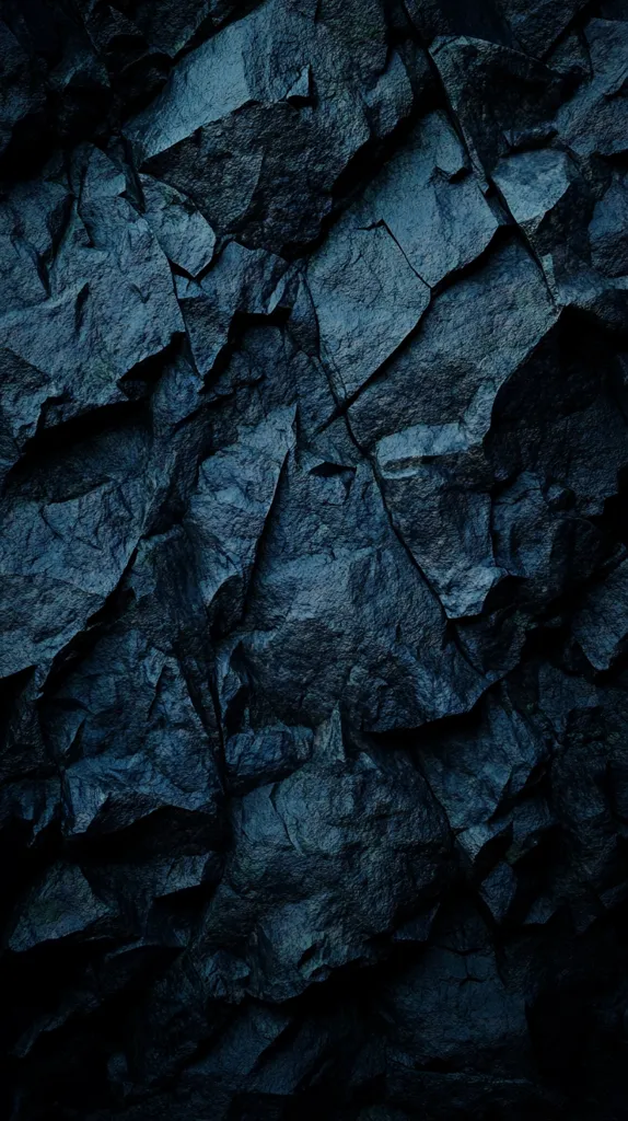 The image shows a close-up of a dark blue rock face. The rock is rough and textured, with many cracks and crevices. The image is lit in a way that creates deep shadows and highlights, giving the rock a dramatic and imposing look. The dark blue color and the rough texture of the rock create a sense of mystery and power.