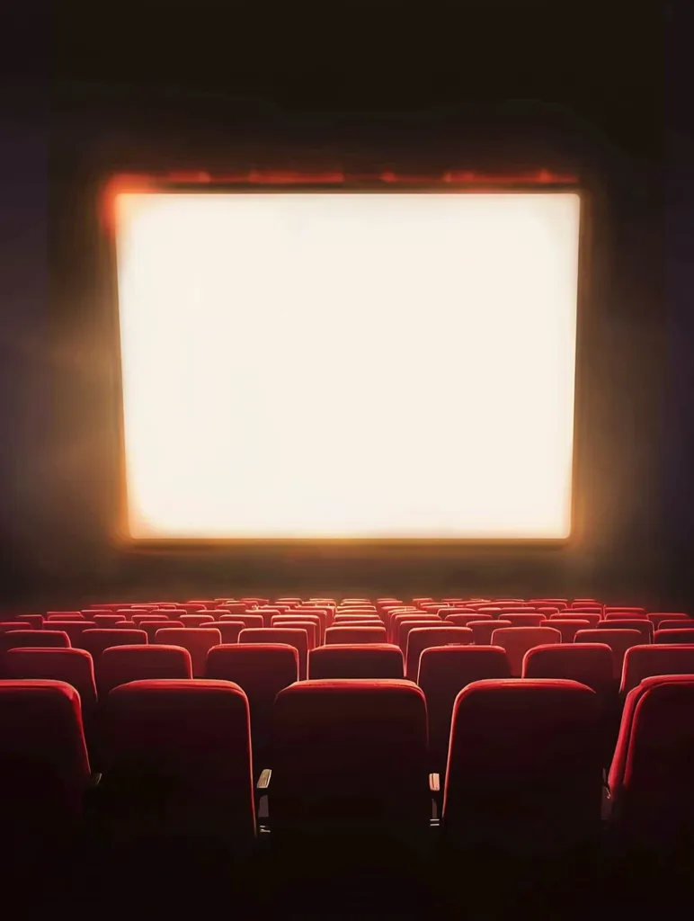 The image shows a movie theater with rows of red seats. A large, bright white screen dominates the back wall. The seats are empty, suggesting the movie has not yet started or has just ended. The darkened room creates a sense of anticipation or quiet contemplation.  A few spotlights illuminate the screen and seats, emphasizing their importance. The image evokes the familiar feeling of being in a movie theater, ready for an immersive cinematic experience.