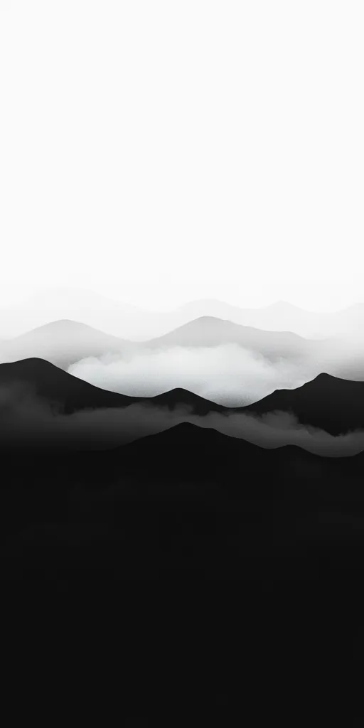 The image is a black and white landscape shot, featuring a mountain range shrouded in fog. The fog creates a sense of mystery and tranquility, as it rolls over the peaks and valleys. The image is minimalist, with a simple composition that emphasizes the beauty of the natural world. The white space at the top of the image adds to the feeling of openness and serenity.