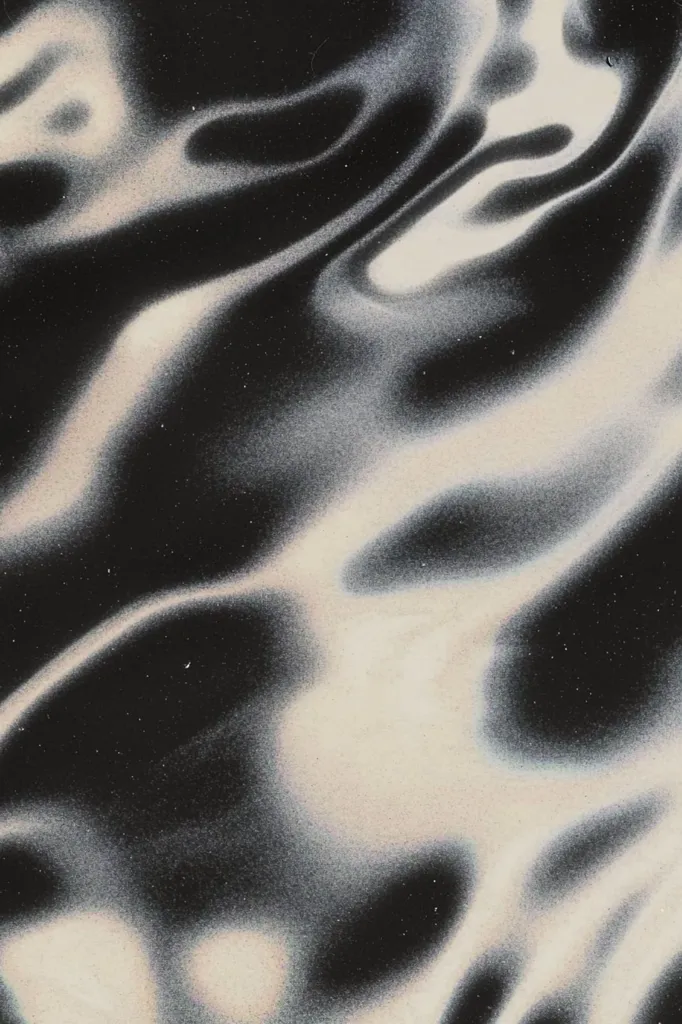 The image shows an abstract, swirling pattern in shades of black, white, and grey. The colors blend seamlessly, creating a sense of movement and fluidity. The surface appears to be slightly textured, with a subtle graininess that adds depth to the design. The overall effect is one of ethereal beauty and subtle elegance.
