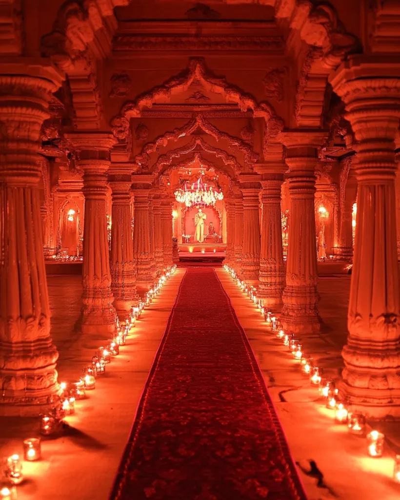A long, red carpet stretches down the center of a brightly lit, ornate hallway.  The hallway is lined with columns and arches, with flickering candles casting warm, orange light on the walls and floor.  The end of the hallway disappears into a golden glow.  The scene is elegant and inviting.