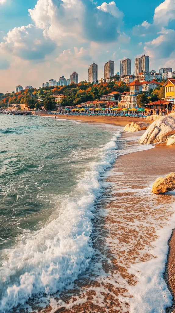 A picturesque beach scene unfolds with a sandy shoreline kissed by foamy turquoise waves. Lush greenery adorns the hillside, where a charming coastal town boasts a line of white buildings nestled under a vibrant blue sky. Fluffy white clouds drift lazily across the canvas, casting soft shadows on the idyllic landscape.