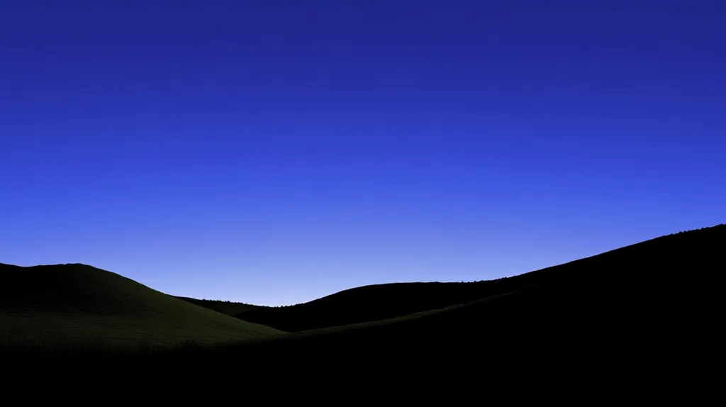 The image shows a silhouette of rolling hills against a vibrant blue sky. The sky is clear and devoid of clouds, creating a sense of vastness and tranquility. The hills are dark and imposing, their outlines stark against the bright sky. The image is a simple yet powerful representation of the beauty of nature.