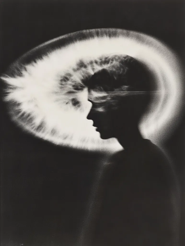 The image is a black and white photograph of a person's head and shoulders. The subject's face is obscured by a large, white, circular shape that appears to be a halo or a spotlight. The image is dark and mysterious, giving the impression of a person caught in a moment of intense thought or emotion.