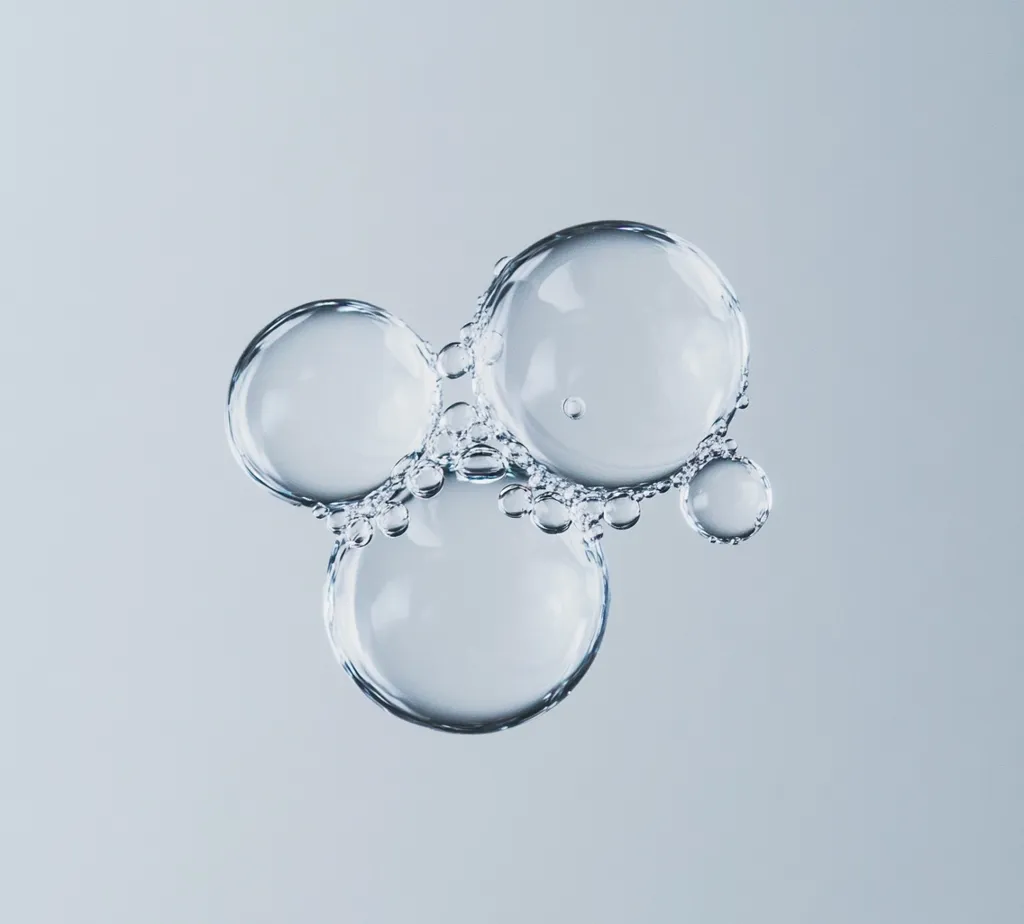 Here's a description of the image:

The image shows a cluster of translucent bubbles against a light gray background.  The bubbles are various sizes, with three prominent larger bubbles forming the main cluster.  Smaller bubbles cling to the larger ones, creating a sense of interconnectedness. The overall impression is one of lightness, purity, and a delicate balance. The lighting is even, highlighting the smooth surfaces and the internal reflections within the bubbles.