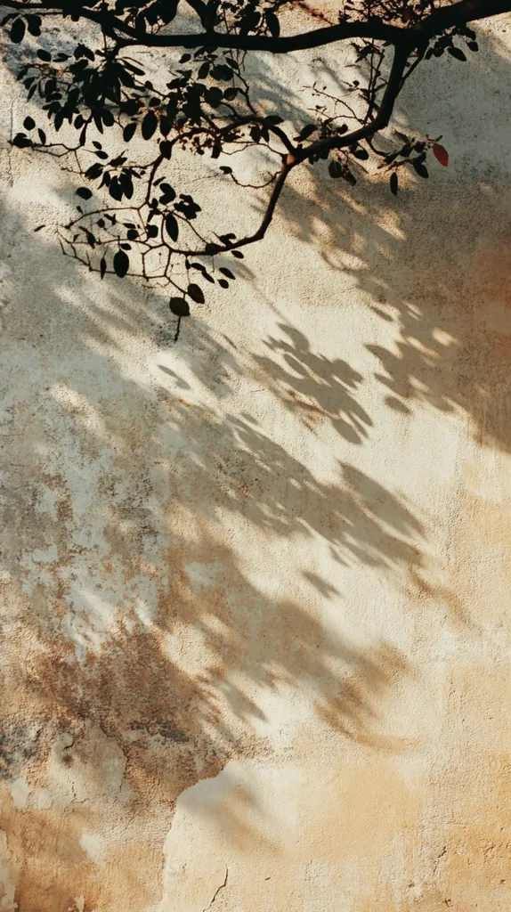Here's a description of the image:

The photograph showcases the interplay of light and shadow on a textured wall. A tree branch, laden with leaves, stretches across the upper portion of the frame, casting a dappled shadow across the wall below. The wall itself is a light beige, exhibiting signs of age and weathering with patches of discoloration and cracking. The shadows mimic the delicate shapes of the leaves, creating a subtle, artistic contrast against the wall's organic texture. The overall mood is serene and evocative of a warm, possibly Mediterranean, climate.
