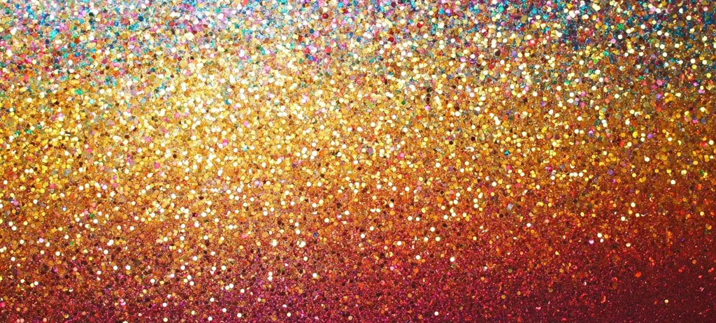 The image shows a vibrant, glittering texture.  Millions of tiny, iridescent particles create a gradient effect, transitioning from light teal and gold at the top to deep crimson at the bottom.  The gold tones dominate the center, with hints of pink, orange, and red throughout. The overall effect is one of intense sparkle and shimmer, suggesting festivity or celebration.