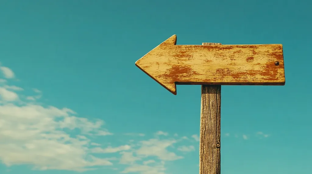 A weathered, blank wooden arrow sign points left against a vibrant teal sky.  Soft, fluffy white clouds drift lazily across the upper left of the frame. The arrow is affixed to a rustic, grey wooden post.  The overall tone is nostalgic and evokes a sense of journey or direction, leaving the destination open to interpretation.  The blank sign invites the viewer to fill in the meaning.