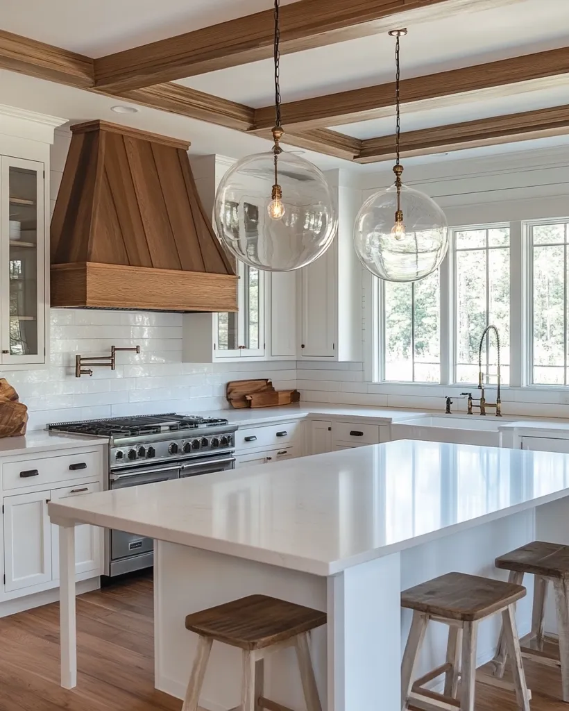 A bright, modern kitchen features white cabinetry, a large quartz island with wooden stools, and a wood-paneled range hood.  Two large glass globe pendant lights hang above the island, illuminating the space.  The hardwood floors and exposed wood ceiling beams add warmth to the clean, white aesthetic.  Large windows offer abundant natural light.