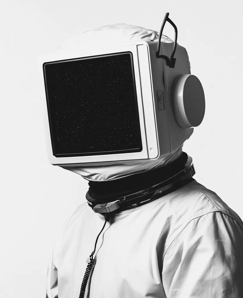 A monochromatic image depicts a figure in a spacesuit-like garment.  The head is covered by a white hood with an old-fashioned computer monitor as a faceplate. The screen displays a starry night sky. A cord extends from the monitor, adding a surreal and technological element to the astronaut-like figure. The overall aesthetic is minimalist and evocative of science fiction.