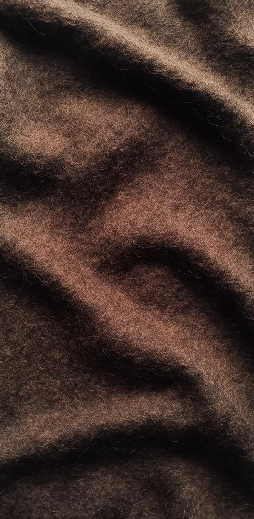 A close-up shot reveals a richly textured fabric, dark brown in color.  The material appears soft and fluffy, with subtle waves and folds creating depth and shadow. The surface is uniformly hairy, enhancing its plush texture. The overall impression is one of luxurious softness and warmth.