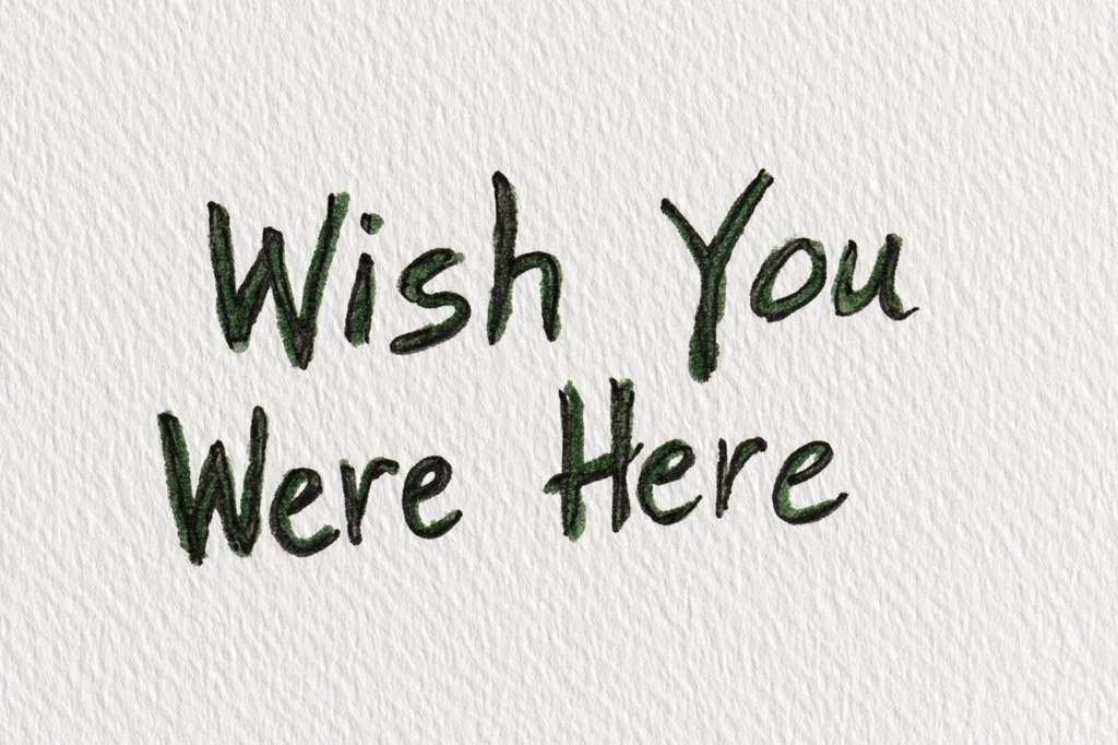 The image shows the handwritten phrase "Wish You Were Here" on a textured white background.  The words are written in a casual, slightly slanted script with dark green ink.  The text is centered on the page, conveying a message of longing or absence. The textured paper adds a subtle, handmade feel to the image.