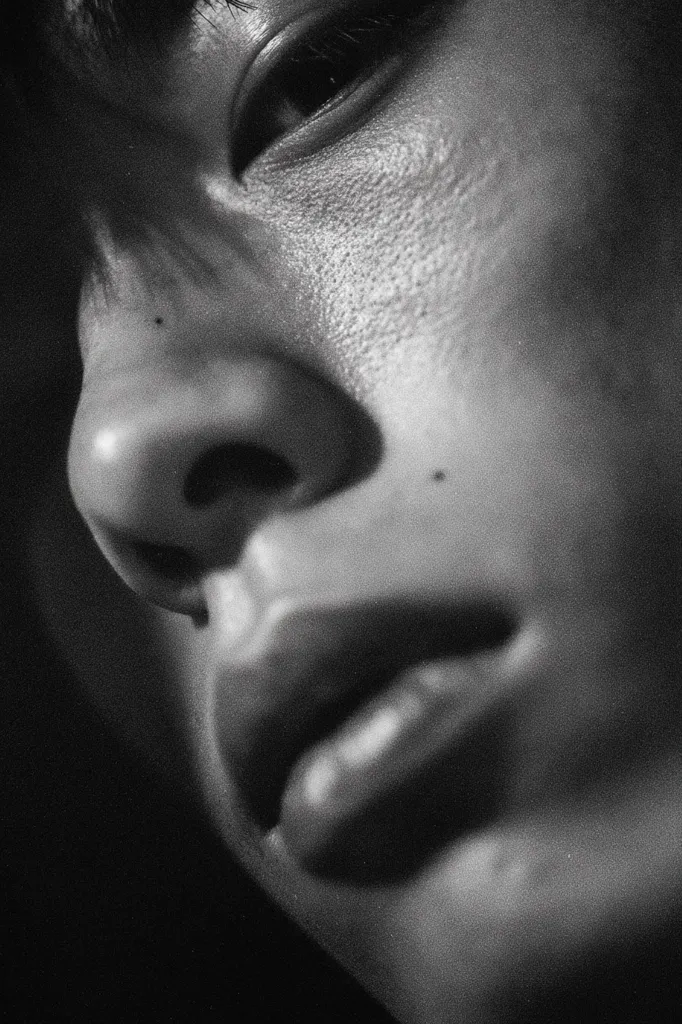 A close-up, black and white photograph captures a person's face in profile.  The image focuses on the nose, mouth, and eye, highlighting the texture of the skin.  The lighting is dramatic, creating shadows and emphasizing the contours of the face. The overall mood is intimate and slightly melancholic.