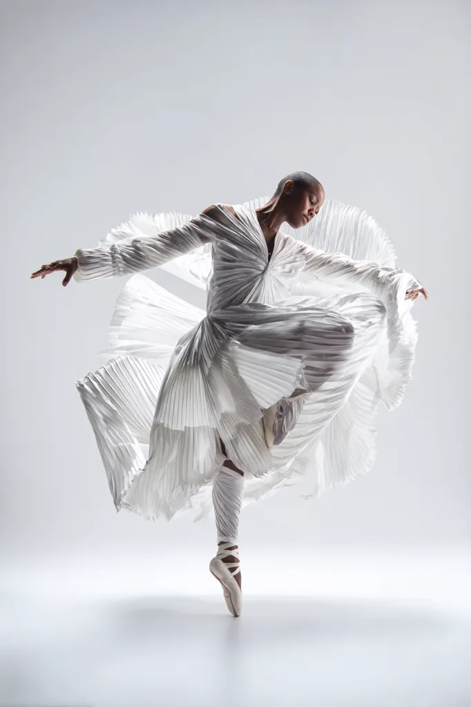 A Black ballerina, poised in a graceful arabesque, is captured mid-leap against a stark white backdrop.  She wears a flowing, pleated white gown that billows around her as she rises en pointe. The image emphasizes elegance, movement, and the power of dance, showcasing both the dancer's skill and the artistry of the costume design.  The minimalist setting focuses all attention on the dancer's form and expression.