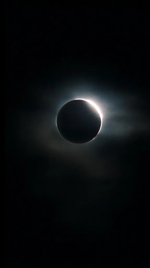 A breathtaking image captures the totality of a solar eclipse. The dark silhouette of the moon completely obscures the sun, creating a dramatic contrast against the subtly luminous corona.  A faint, ethereal glow surrounds the moon, a celestial spectacle of light and shadow. The dark sky provides a stark backdrop to this awe-inspiring event.