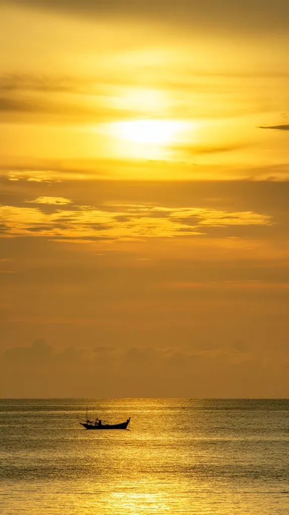 A lone fishing boat rests on a calm sea under a breathtaking sunset. The sky blazes with vibrant gold and orange hues, the sun a bright disc near the horizon.  The silhouette of the boat against the radiant sky creates a serene and picturesque scene, capturing the tranquility of the golden hour.