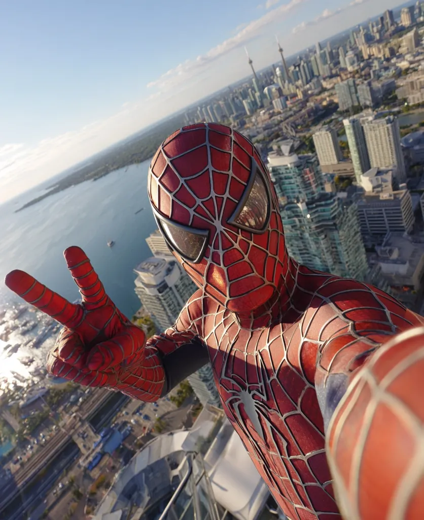 A Spider-Man cosplayer takes a selfie from a Toronto skyscraper, showcasing the city skyline and Lake Ontario in the background.  The cosplayer's suit is highly detailed, and they flash a peace sign. The CN Tower is visible in the distance, creating a dramatic backdrop to this superhero-themed photograph.  The image suggests excitement and adventure.
