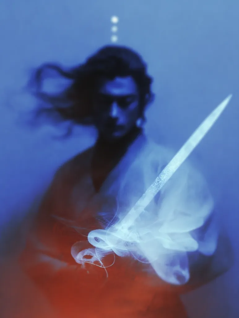 A stylized portrait of a person, possibly a samurai, with long dark hair blowing in the wind. They are holding a sword, which appears to be dissolving into a swirling, ethereal cloud of white smoke. The background is a cool blue, contrasting with warmer red-orange tones in the foreground.  The overall effect is dreamlike and mysterious.